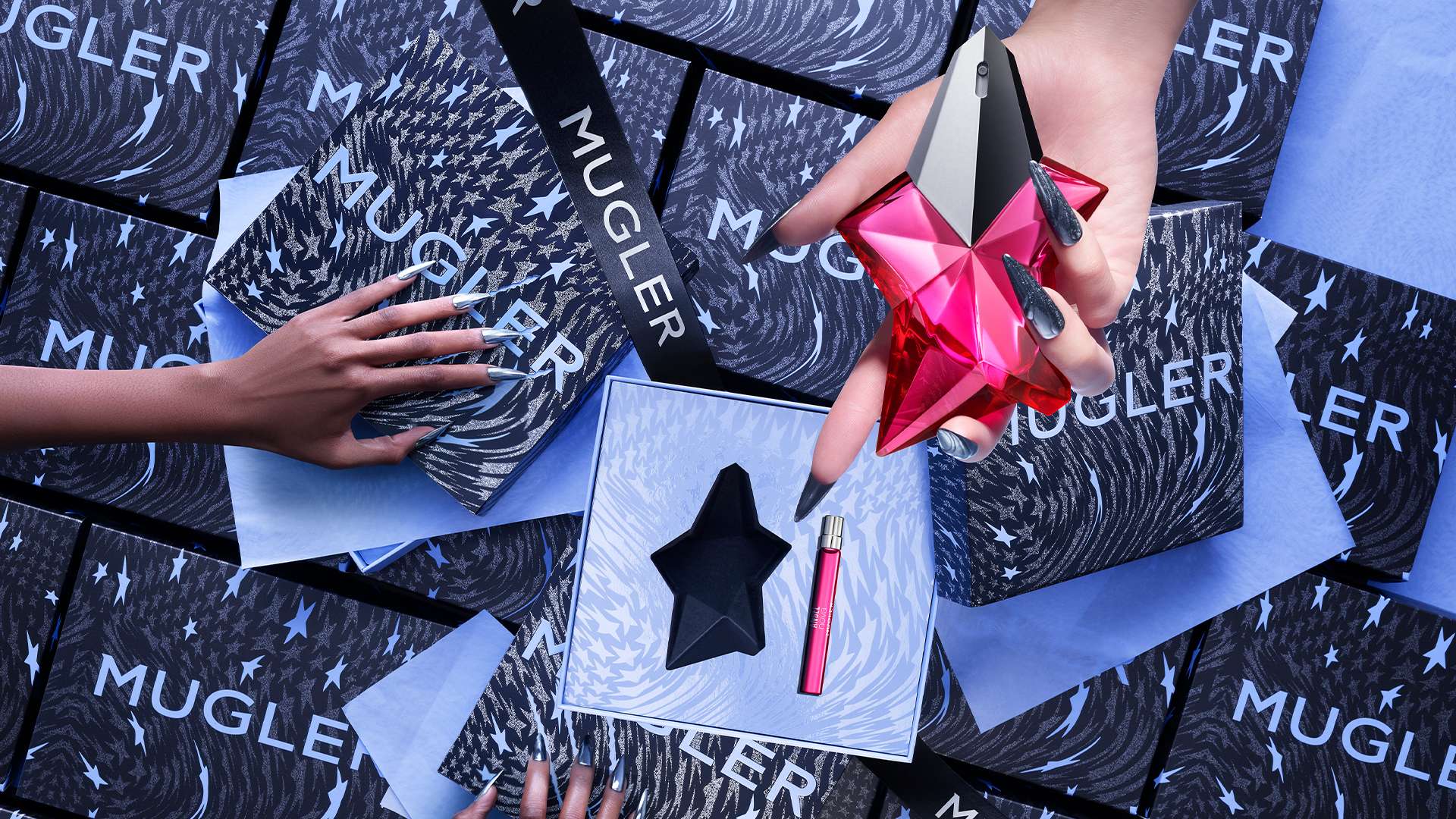 Main subject : Flacon de parfum Mugler en forme d’étoile, posé sur une boîte avec d'autres flacons et papiers d'emballage.