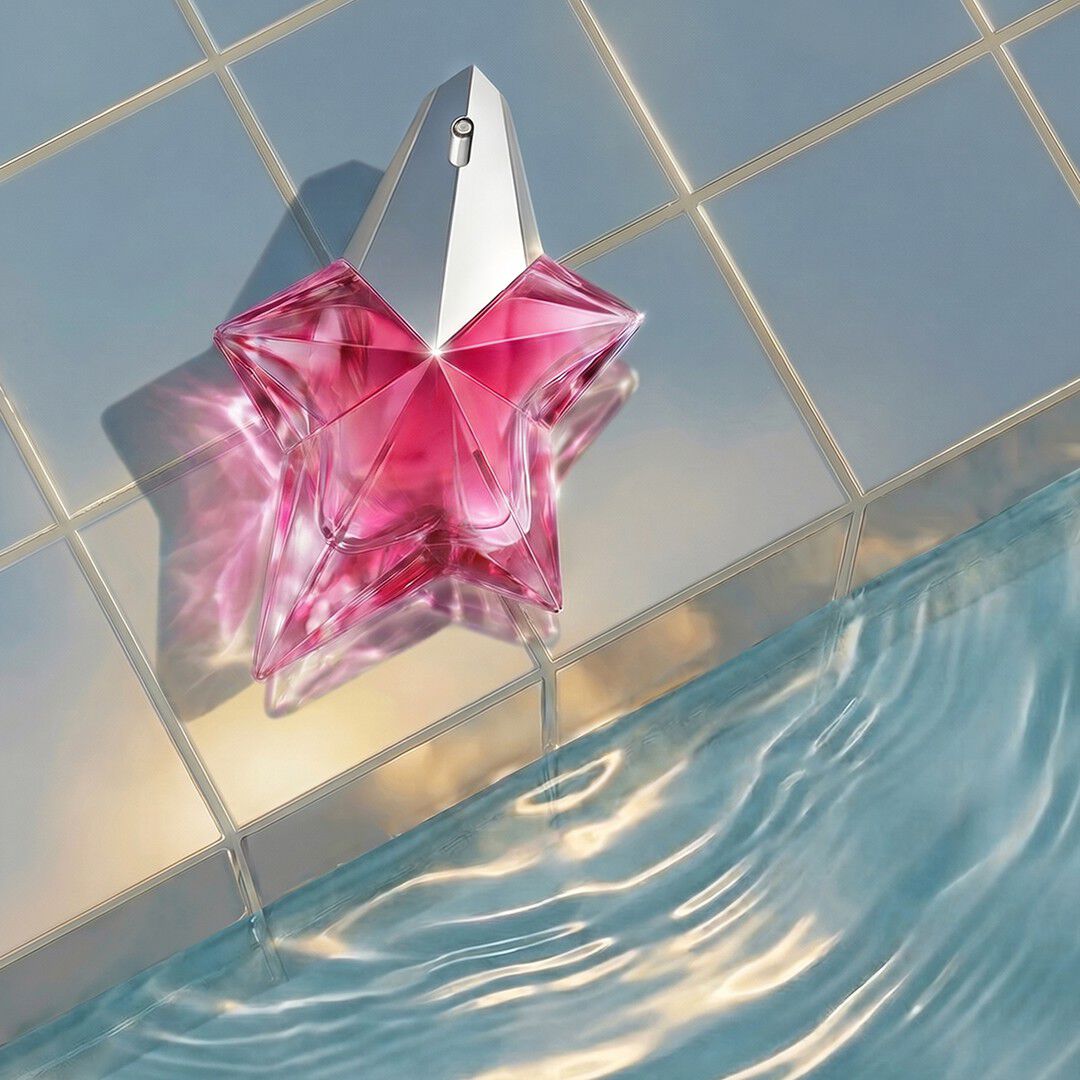 Le flacon en forme d étoile de Mugler Angel Nova, d un rose vif, repose au bord d un bassin aux eaux ondulantes, sur un fond de carreaux clairs et brillants.