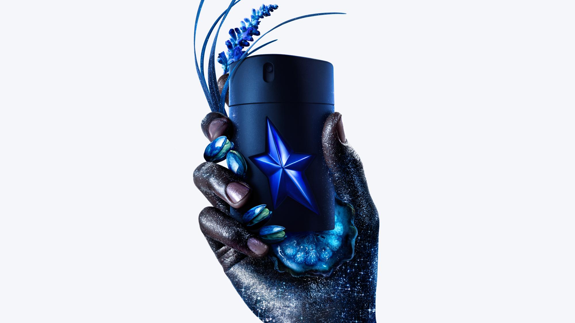 Flacon de parfum étoilé tenu par une main ornée, entouré de fleurs et de textures galactiques.