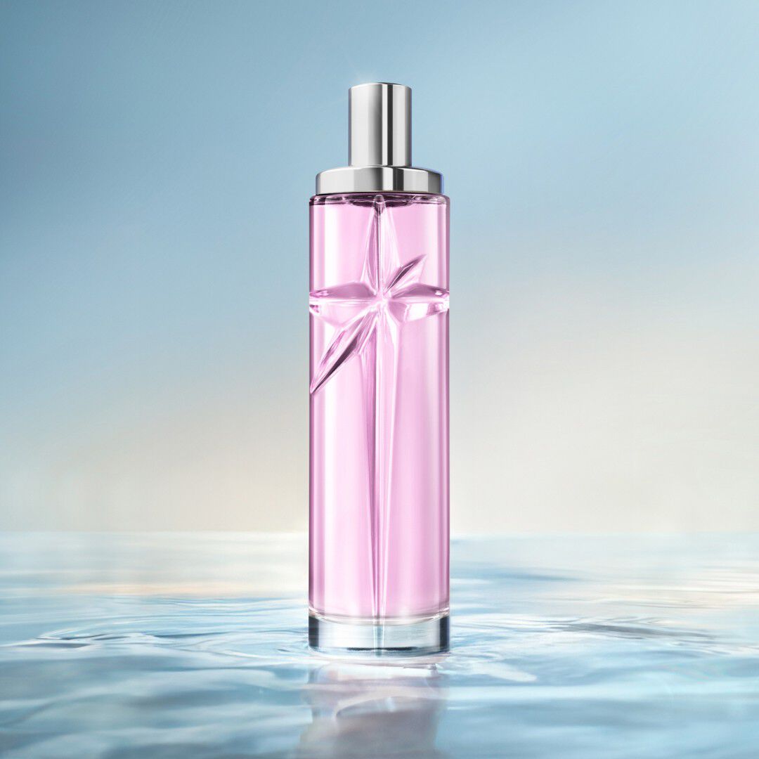 Un flacon de recharge rose Starlicious de Mugler posé dans une eau peu profonde et miroitante, sur un fond bleu lumineux.