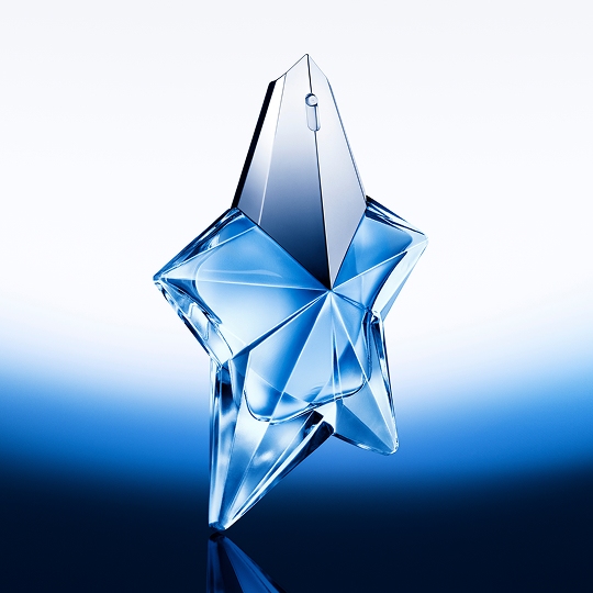 Flacon en forme d'étoile, en verre transparent et bleu, reflétant la lumière sur un fond dégradé bleu clair.