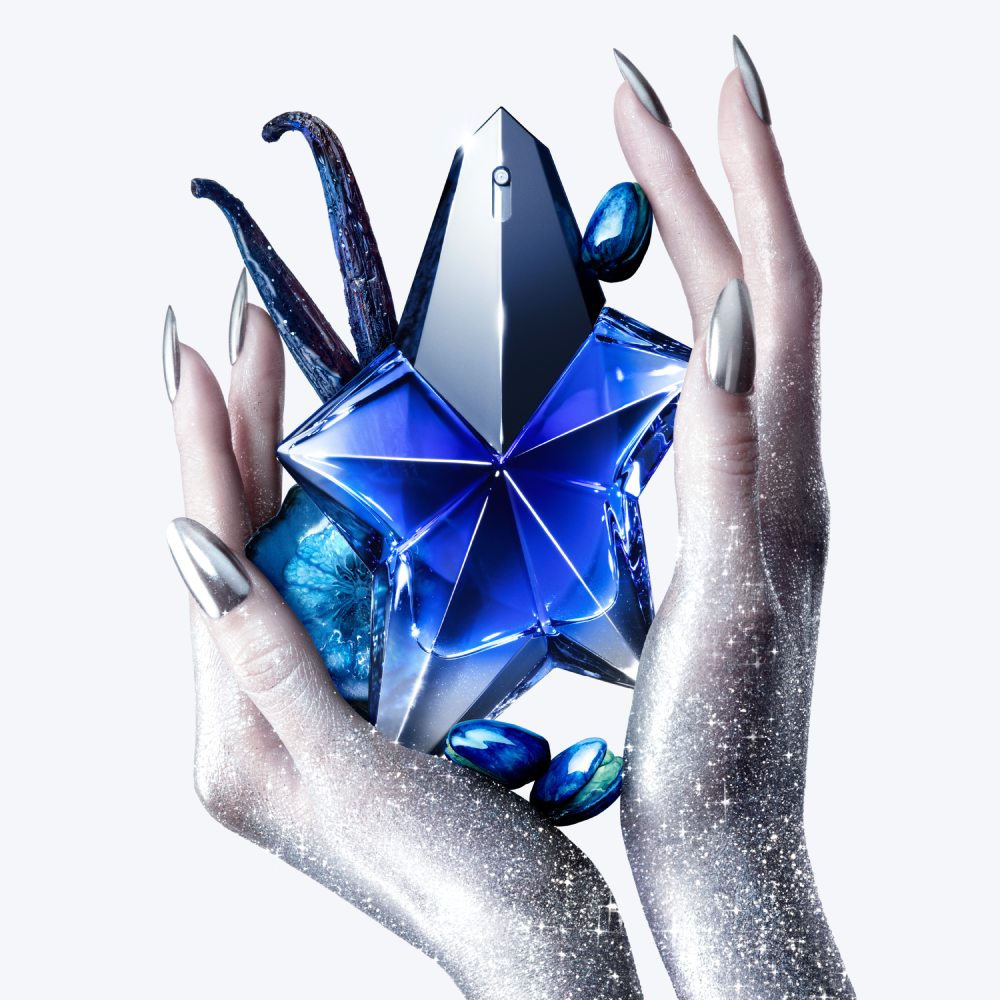 Flacon de parfum en forme d'étoile, tenu par des mains scintillantes, entouré de pierres bleues. Élégance et mystère.