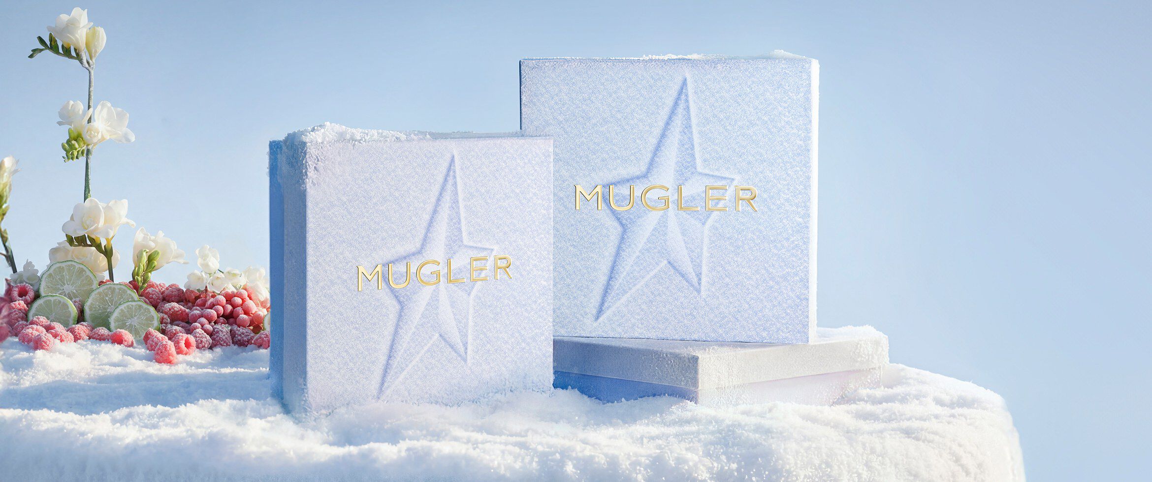 Deux coffrets cadeaux de Noël Mugler, de couleur bleu glacier et à la texture originale, ornés de motifs d étoiles en relief, se dressant dans un paysage hivernal enneigé.