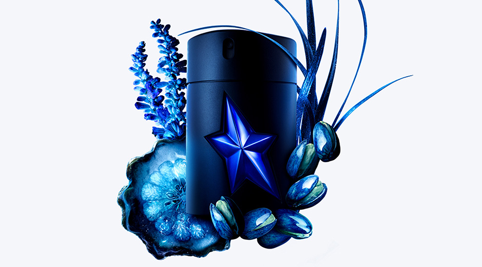 Flacon de parfum bleu avec étoile, entouré d'éléments naturels comme des fleurs et des graines.